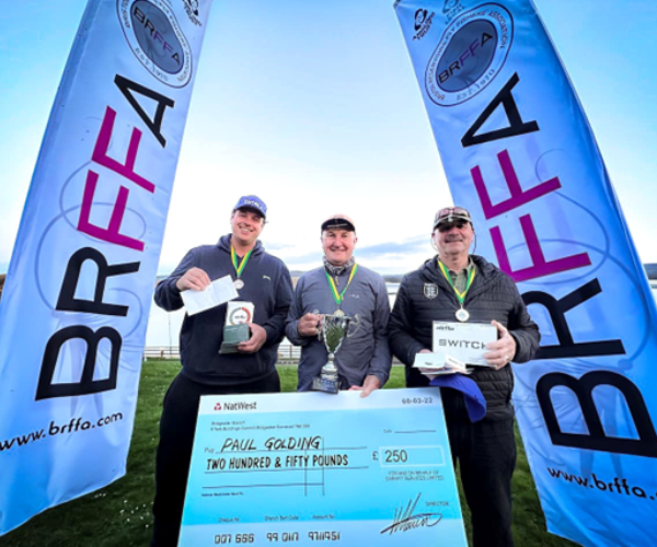 three men posing with a cheque next to a fishing lake