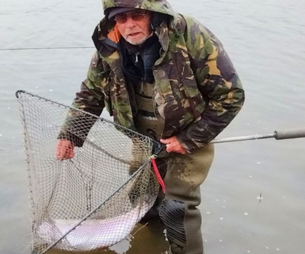 a man in a camouflage coat catching a fish in a net 